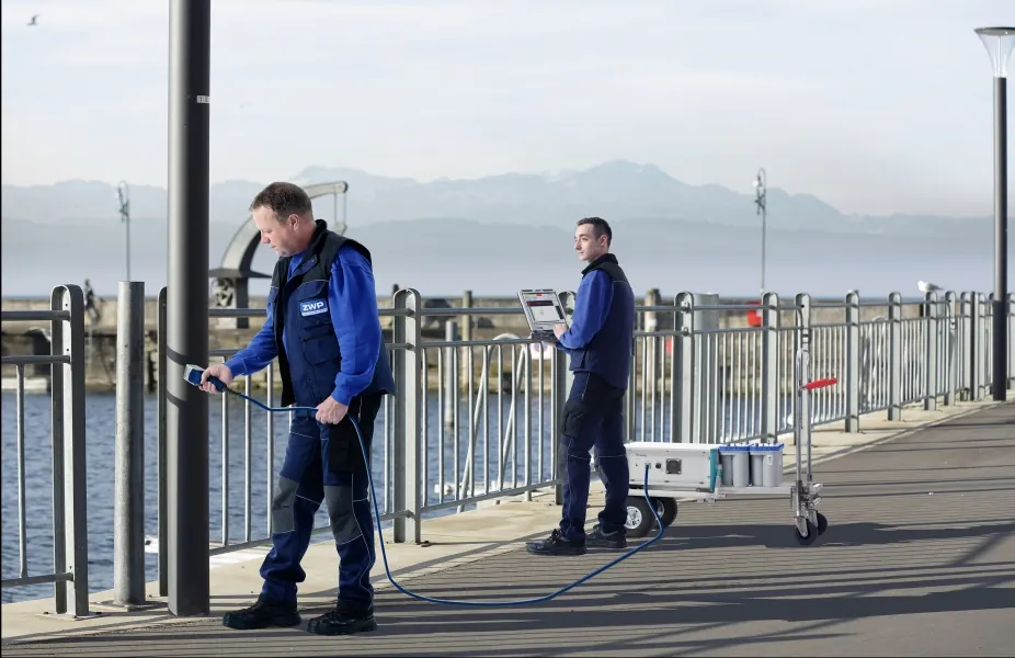 Zwei ZWP-Prüfer prüfen Lichtmaste auf einer Hafenbrücke