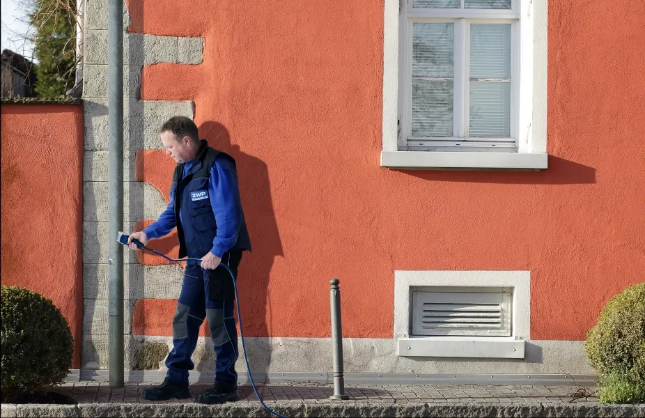 ZWP-Prüfer bei der Standsicherheitsprüfung eines Mastes vor einer Hauswand
